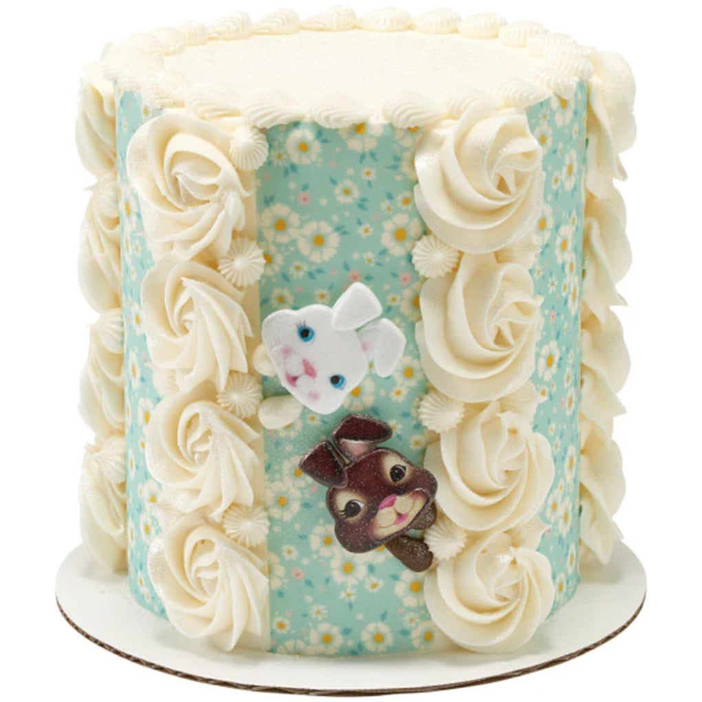Tall Easter cake decorated with blue floral panels, white buttercream rosettes, and white and brown bunny face rings arranged on the front.