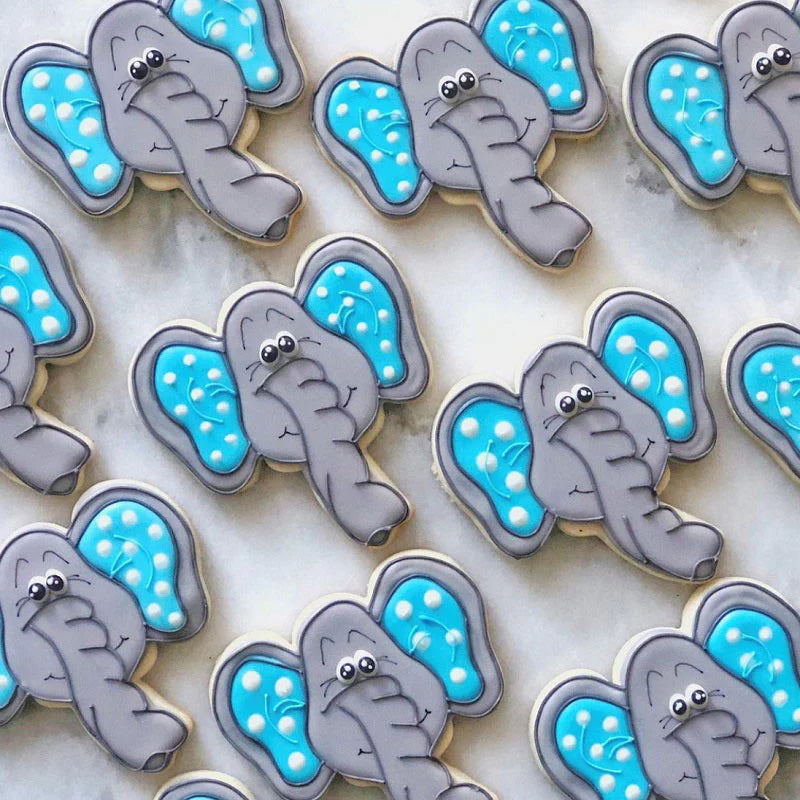 Multiple elephant face-shaped cookies decorated with gray icing, blue ears, and expressive eyes, arranged on a marble surface.