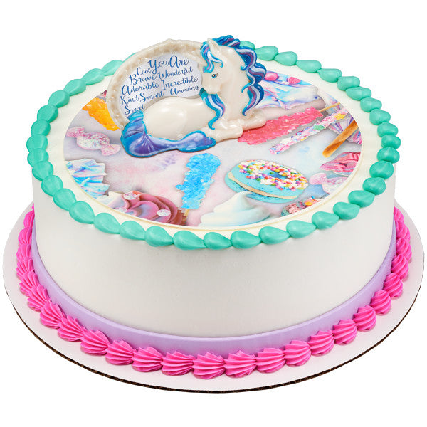Round cake with colorful icing borders, featuring an enchanting unicorn cake topper figurine with pastel mane and tail, surrounded by delightful candy graphics.