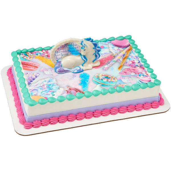 Rectangular cake with whimsical candy-themed graphics, topped by an enchanting unicorn figurine cake decoration, bordered with pastel pink, purple, and turquoise icing.