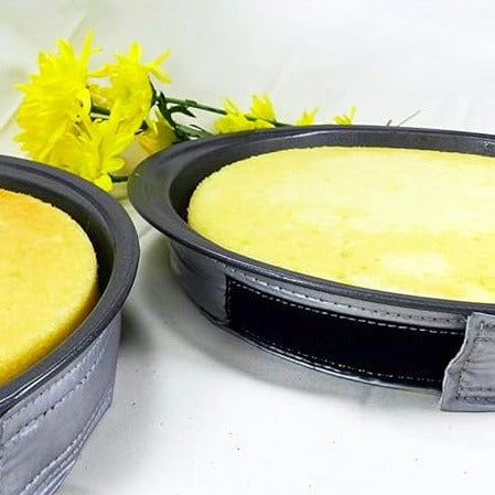 EvenBake cake strips wrapped around round black cake pans filled with yellow cake batter, silver strips secured during baking on a light surface