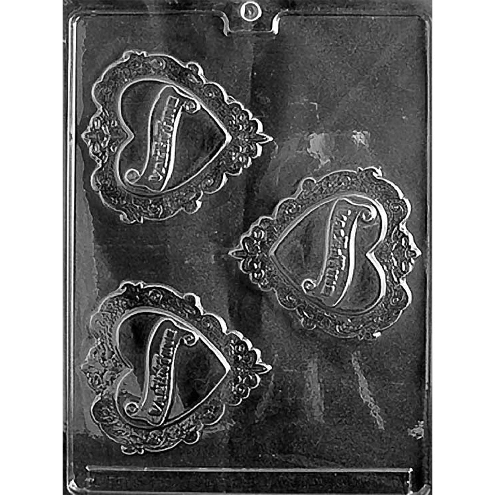 Clear plastic chocolate mold photographed on a black background with three ornate heart-shaped cavities featuring raised decorative borders and a large scripted letter in the center.