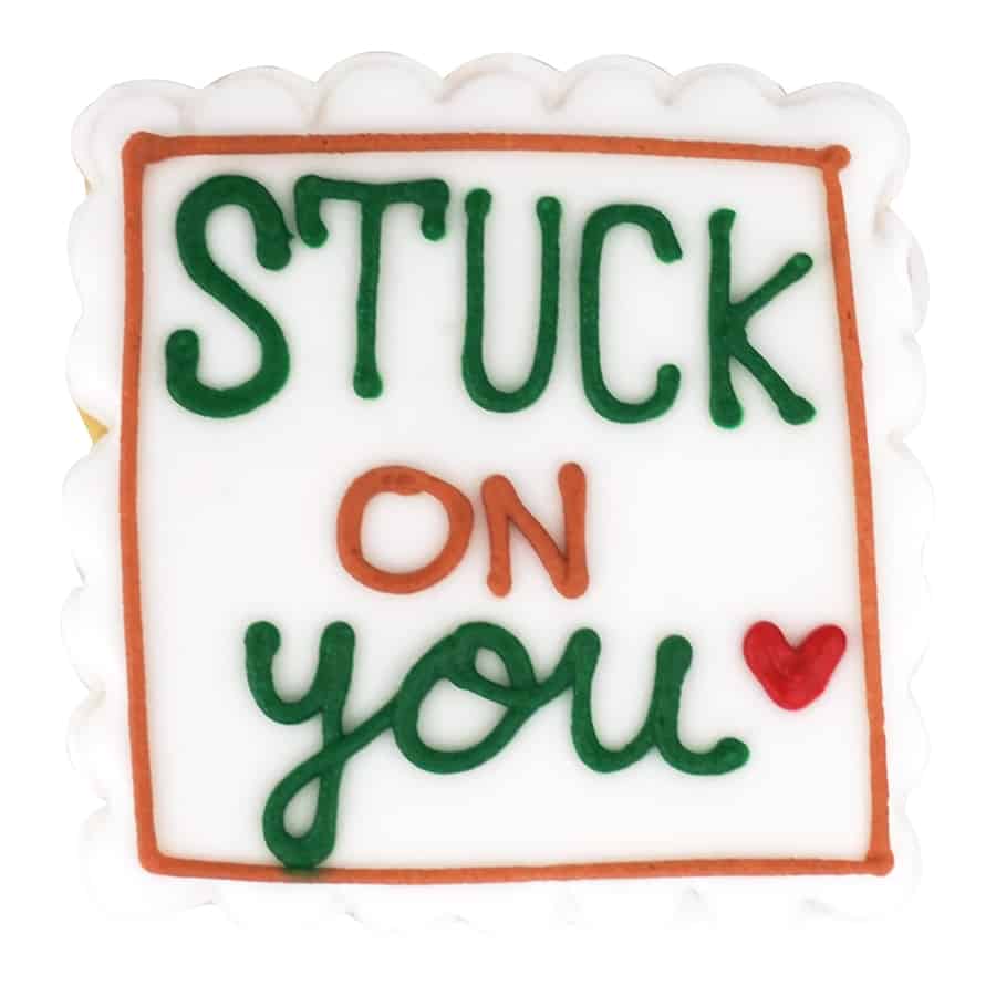 White cookie with green and orange piping reading 'Stuck on You' with a red heart, created with the Square Fluted Cookie Cutter.