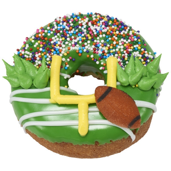 Donut decorated with green icing, piped yellow goalpost, and brown pressed sugar football decoration, accented with white icing lines and colorful sprinkles.