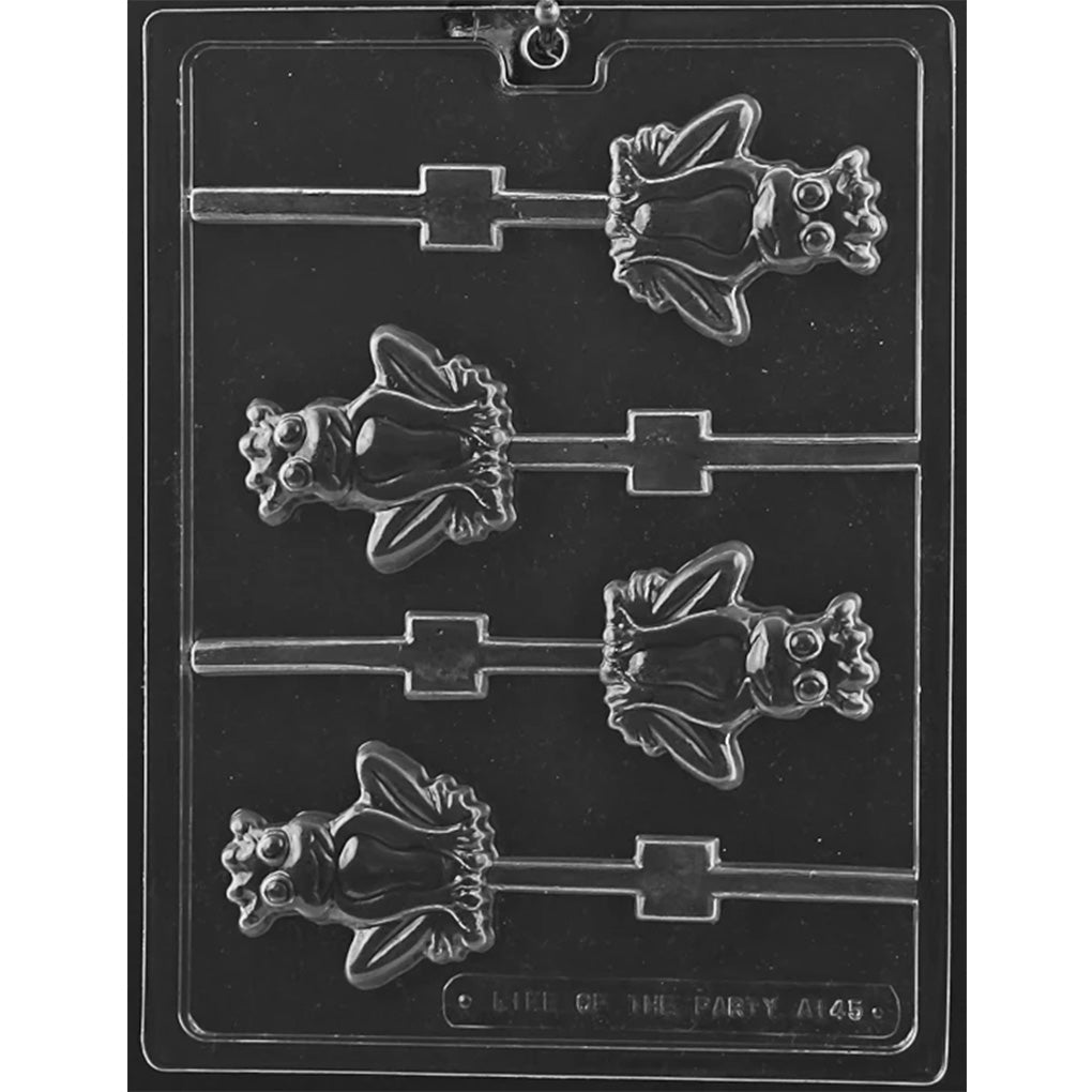 Clear plastic chocolate lollipop mold with four smiling frog prince cavities featuring crowns, large round eyes, webbed feet, and channels for sticks.
