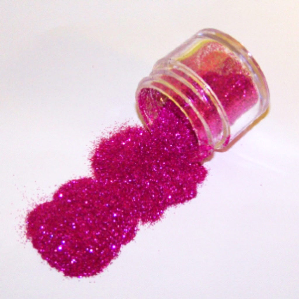 Small clear jar tipped on its side spilling bright glamorous pink glitter dust onto a white surface, with fine sparkling particles visible throughout.