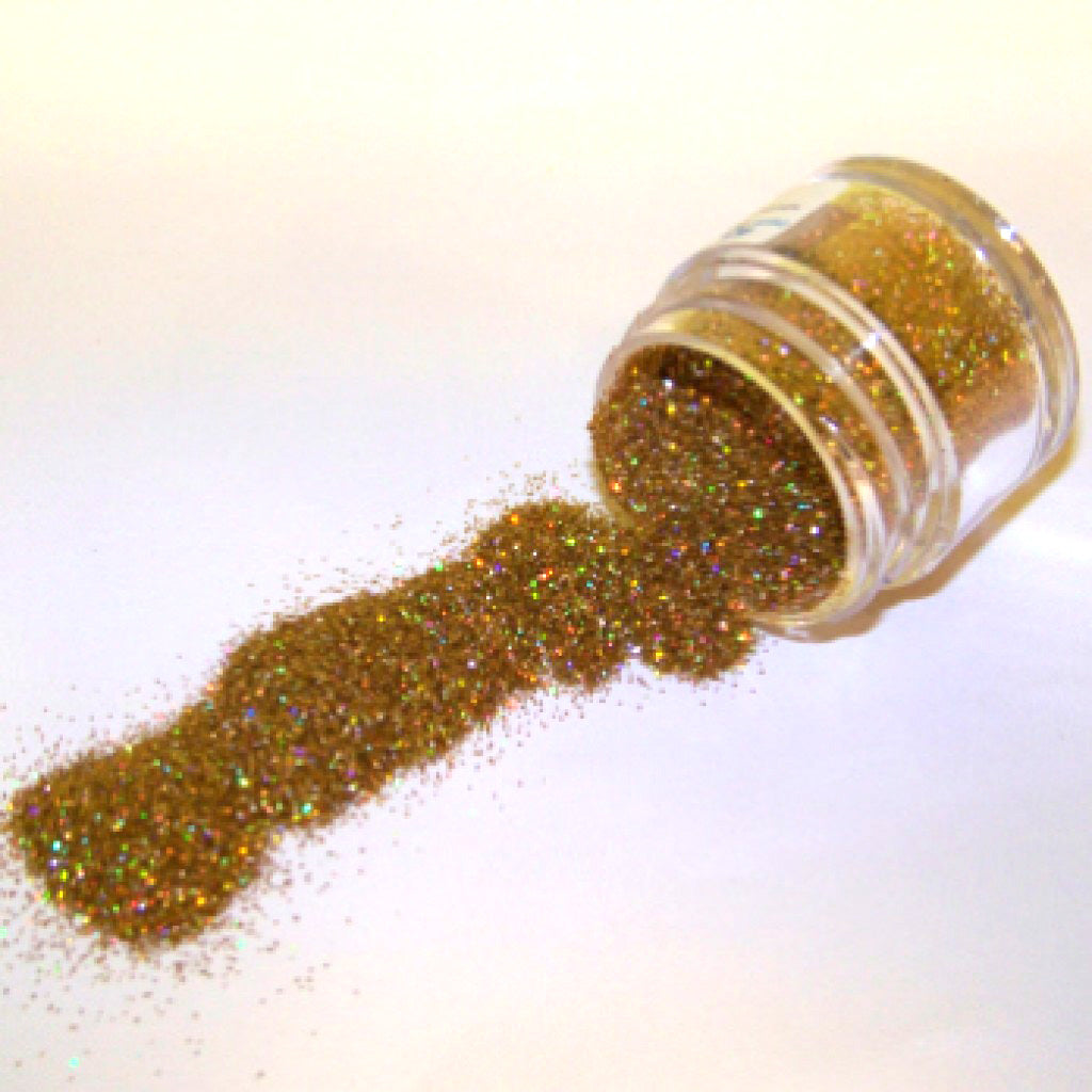 Small clear jar tipped on its side spilling gold hologram glitter dust onto a white surface, with warm golden sparkle and rainbow reflective highlights.