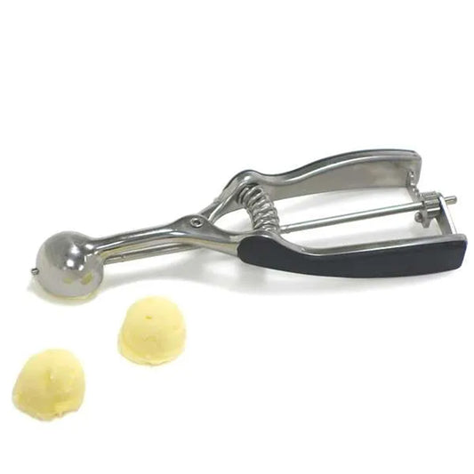 Side view of a #96 stainless steel cookie scoop beside two small scooped butter portions, showing the spring-release mechanism and soft-grip handles.