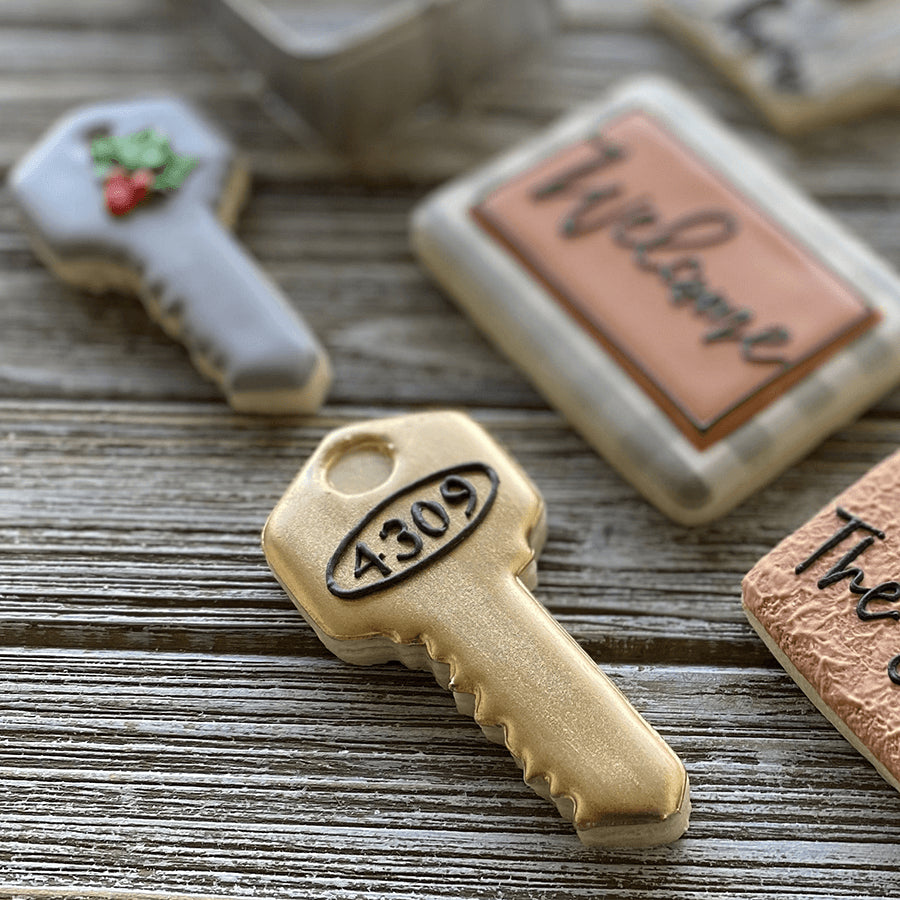 Decorated key-shaped cookies in gold and silver, featuring numbers and details, placed on a rustic wooden surface.