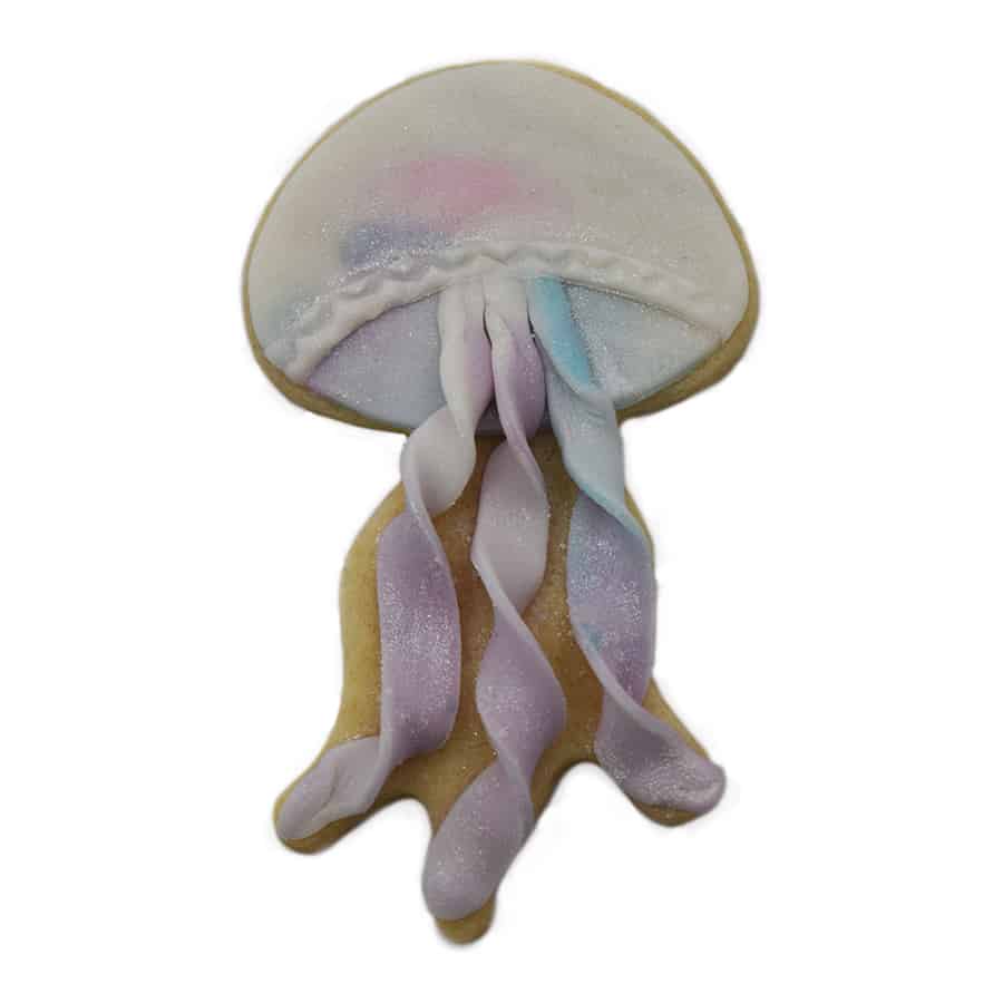 A decorated jellyfish cookie with a white and pastel dome, shimmering ribbon-like tentacles.