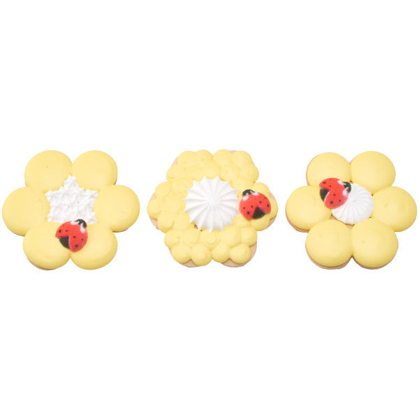 Trio of yellow flower cookies each topped with a piped center and a sugar ladybug for decoration.