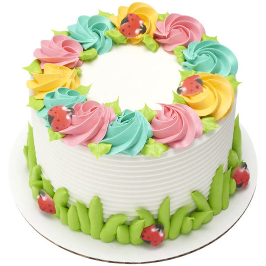 White cake decorated with colorful buttercream rosettes and sugar ladybugs nestled in the flowers and around the base.