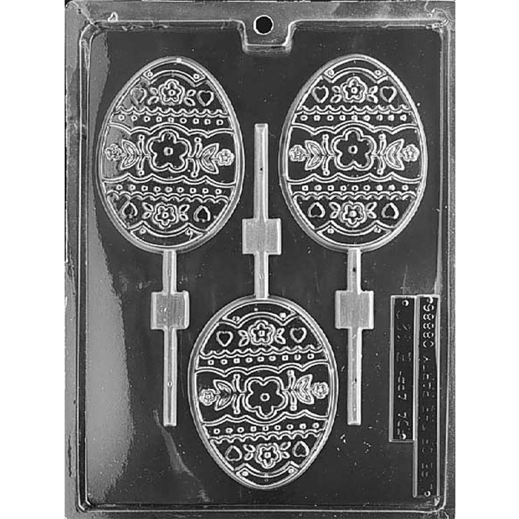 Clear plastic chocolate lollipop mold with three large egg-shaped cavities featuring raised floral, heart, and dotted stripe patterns, each connected to a stick channel on a dark background.