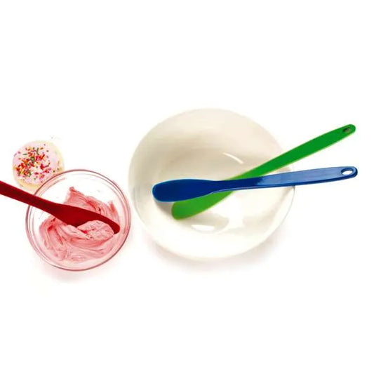 Red, green, and blue spatula scrapers used in mixing bowls with frosting and water