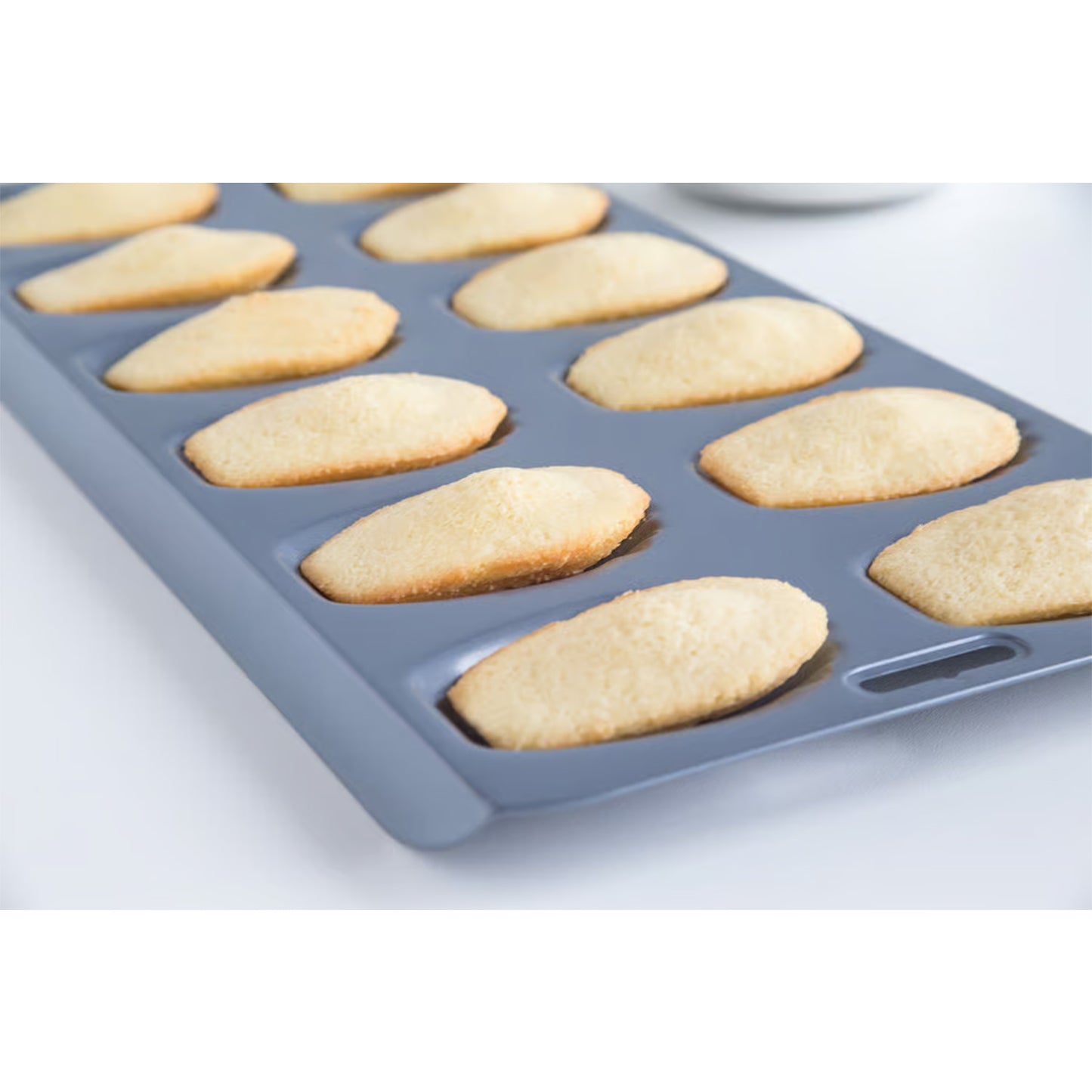 Madeleine pan filled with golden baked madeleines, fresh from the oven, showing uniform shape and texture.