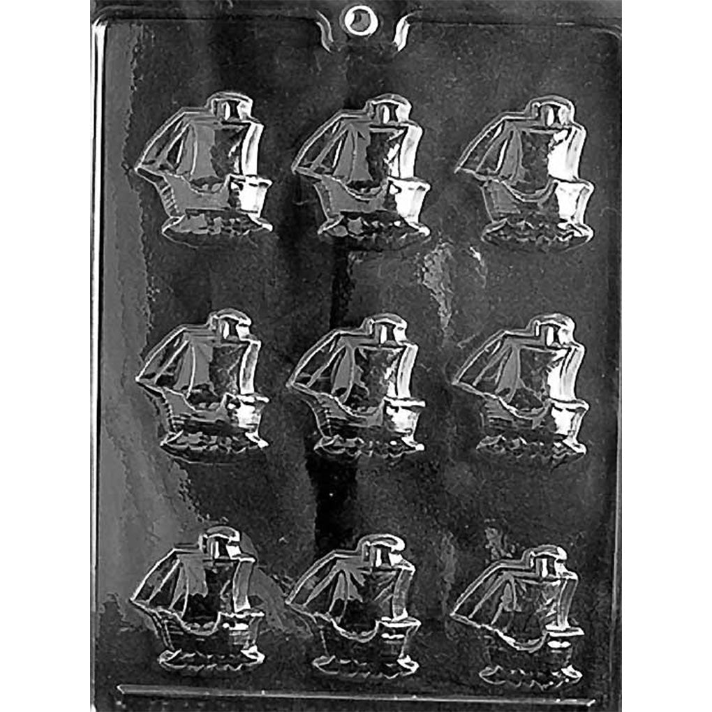 Clear plastic chocolate mold photographed on a black background with nine small sailing ship cavities, featuring raised sail and hull details.