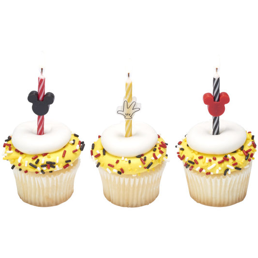 Three cupcakes decorated with yellow frosting, sprinkles, and Mickey Mouse-themed striped birthday candles.