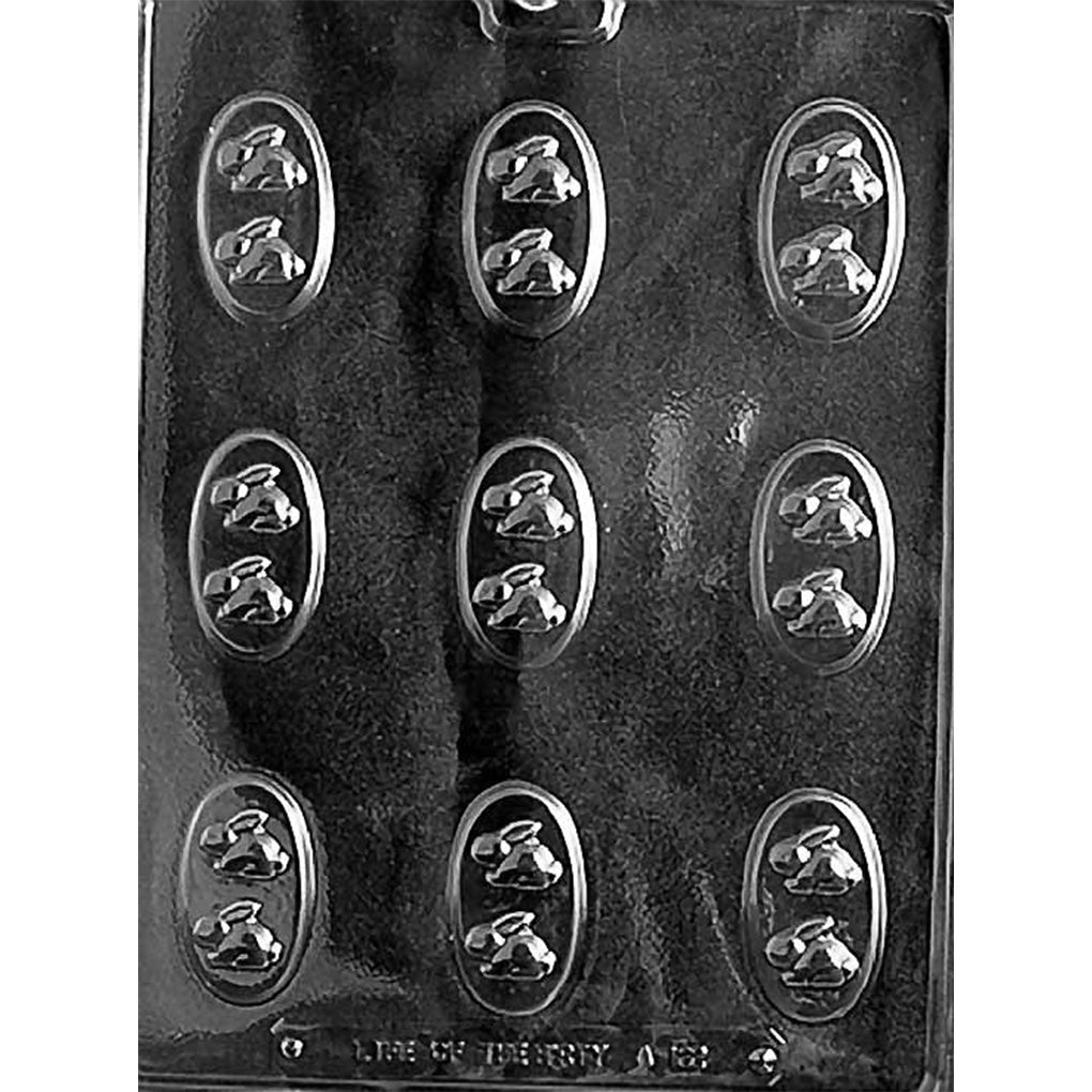Clear chocolate mold with nine small oval cavities, each featuring two tiny bunny shapes, arranged in three rows on a dark background.