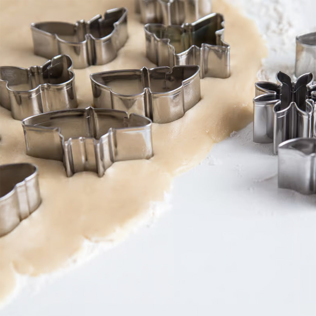 Mini butterfly and flower-shaped cookie cutters placed on rolled-out dough with cutouts visible.