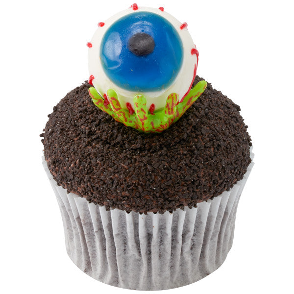 Chocolate cupcake topped with crushed cookie crumbs, a zombie hand pick, and a blue eyeball candy topper.