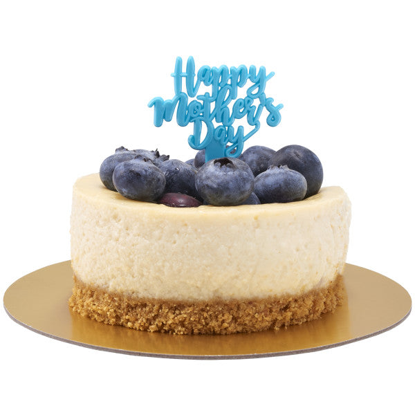 Mini cheesecake topped with fresh blueberries and a teal “Happy Mother’s Day” pick, displayed on a gold cake board.