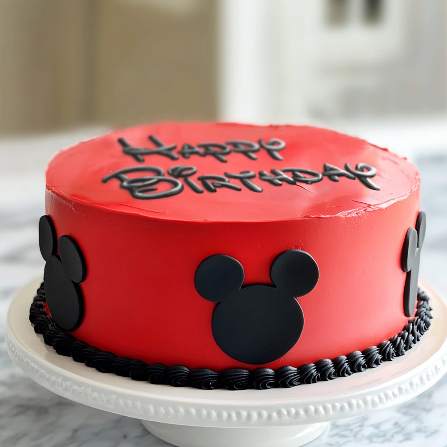 Red birthday cake with black fondant mouse head decorations and "Happy Birthday" written on top.