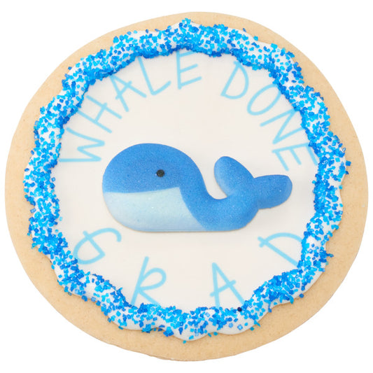 Cookie with blue whale sugar decoration and blue sprinkles, styled with the phrase "Whale Done Grad" for a nautical graduation theme.