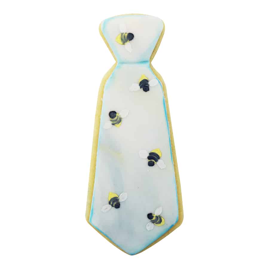 A tie-shaped cookie with a soft watercolor background and tiny bee decorations.