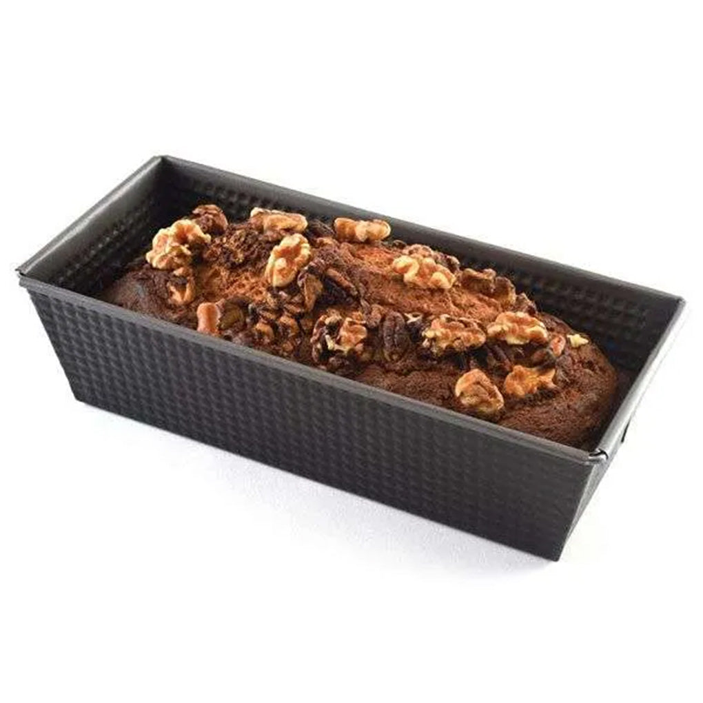 Dark gray corrugated 10-inch loaf pan holding a baked loaf topped with walnuts, photographed at an angle on a white background.