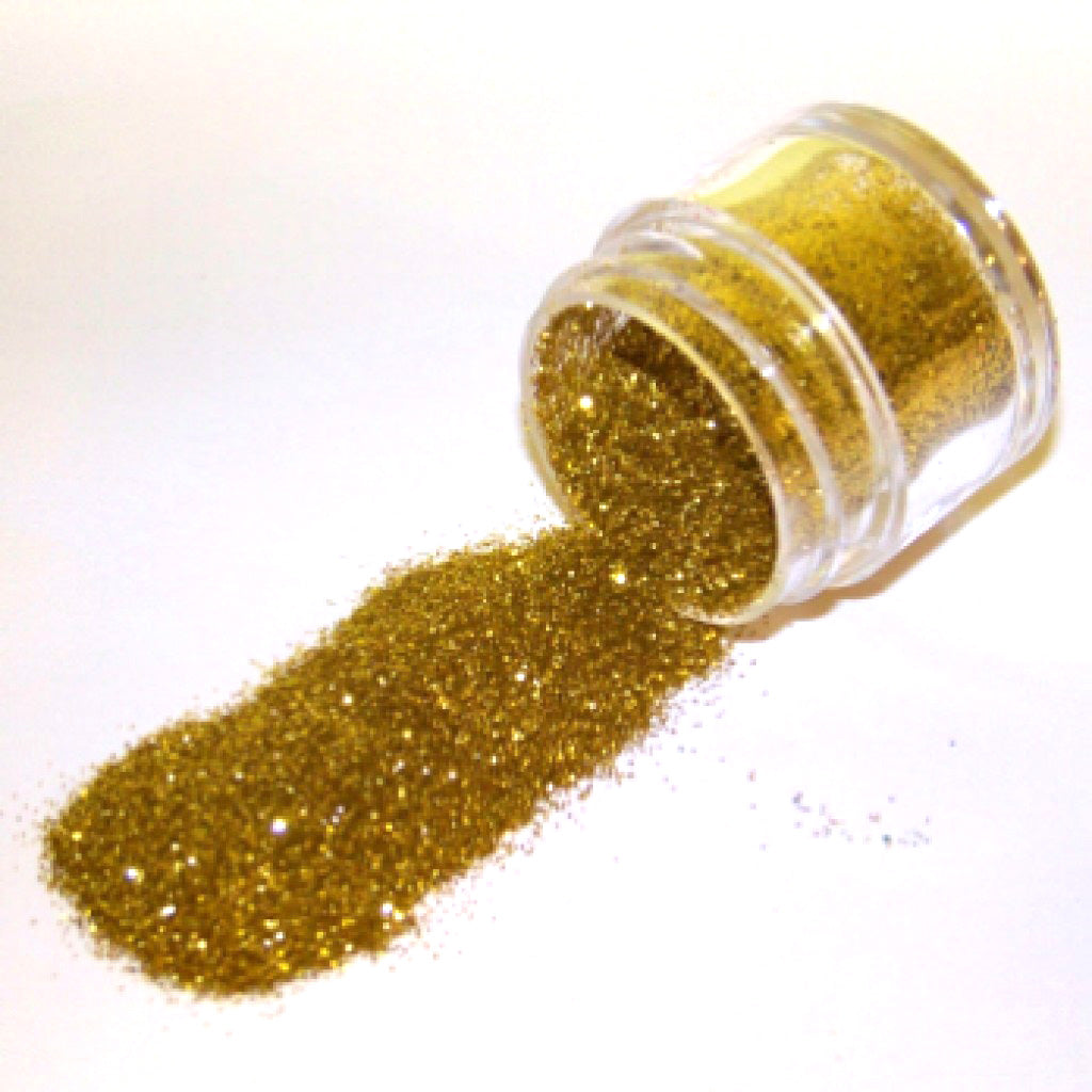 Small clear jar tipped on its side spilling nu gold glitter dust onto a white surface, showing fine metallic gold particles with warm reflective sparkle.