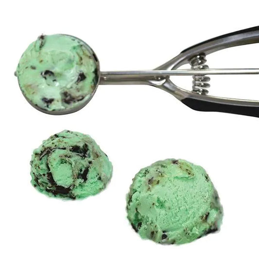 Stainless steel cookie scoop holding mint chocolate chip ice cream above two rounded scoops of green ice cream with chocolate pieces.
