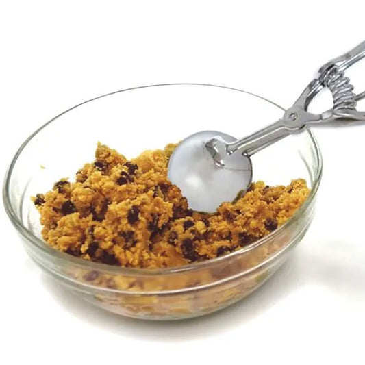 Stainless steel #24 cookie scoop portioning chocolate chip cookie dough from a clear glass bowl.