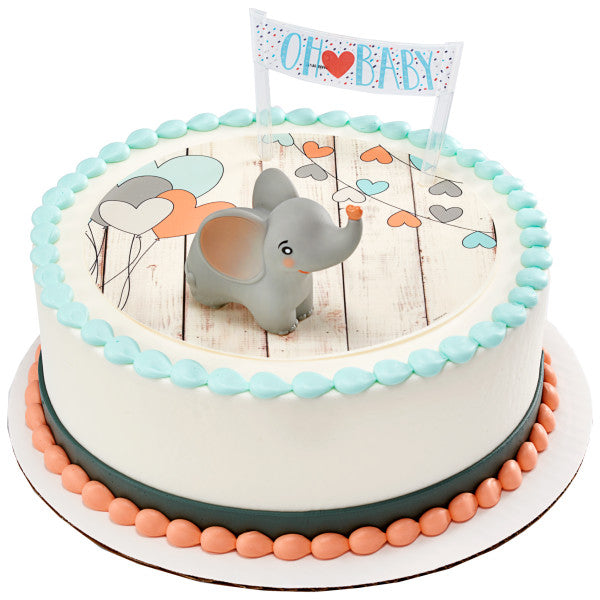 Round baby shower cake with heart and balloon design, decorated with a smiling gray elephant topper and a “Oh Baby” banner.
