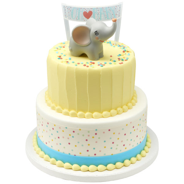 Two-tiered cake with pastel yellow and polka dot design, topped with a baby elephant figurine and “Oh Baby” banner.