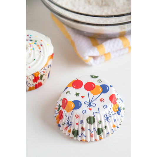 Party balloon baking cups displayed beside a frosted cupcake and mixing bowl