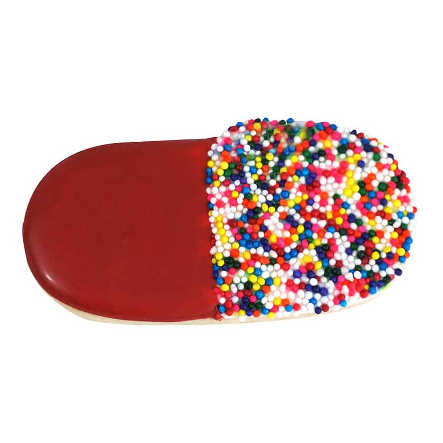 A decorated pill capsule cookie with one half covered in red icing and the other half coated in colorful sprinkles.