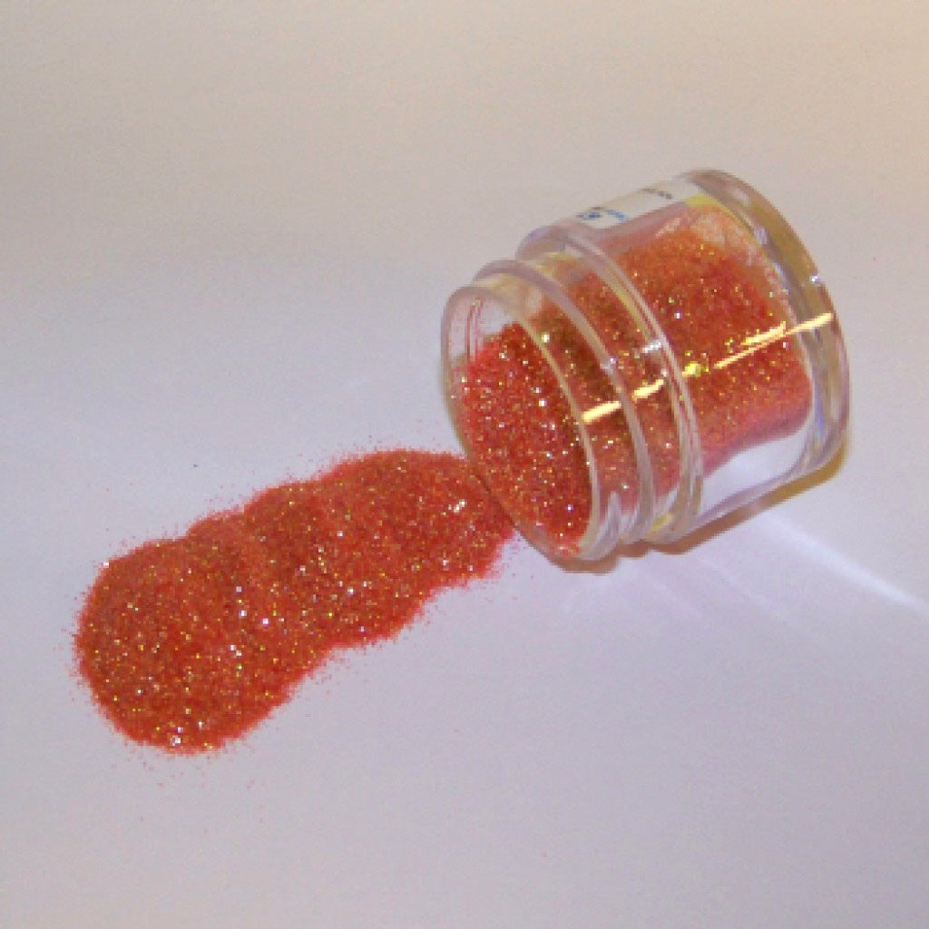 Small jar of pumpkin-orange glitter dust tipped on its side with orange glitter spilled onto a white surface.