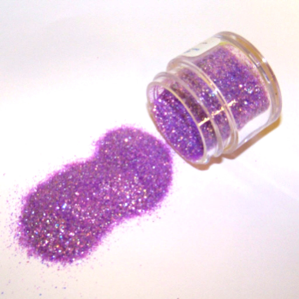 Small clear jar tipped on its side spilling purple rainbow glitter dust onto a white surface, with fine sparkling particles showing an iridescent lavender shimmer.