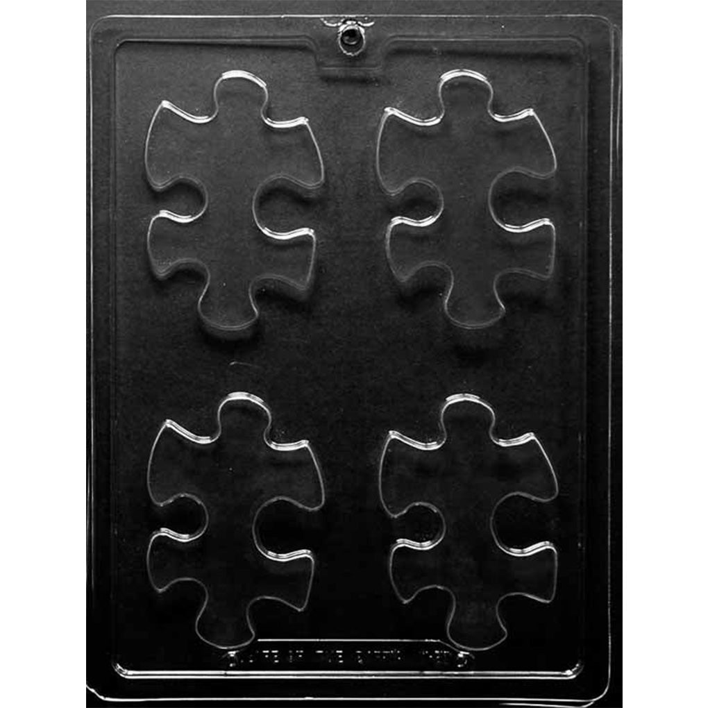 Clear plastic chocolate mold photographed on a black background with four large puzzle piece-shaped cavities arranged in a 2x2 layout.