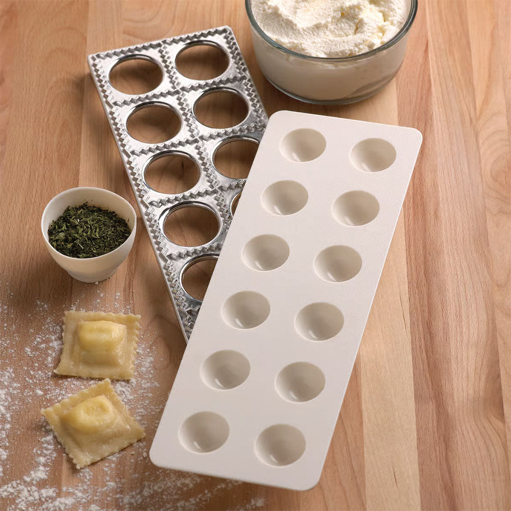 Ravioli maker with press displayed on wooden surface with herbs, ricotta, and freshly made ravioli