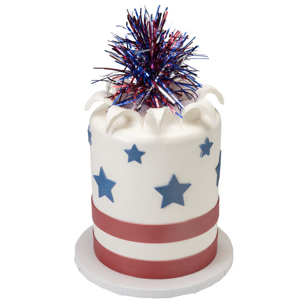 Tall white cake decorated with blue stars, red stripes, and topped with a patriotic pom-pom pick.