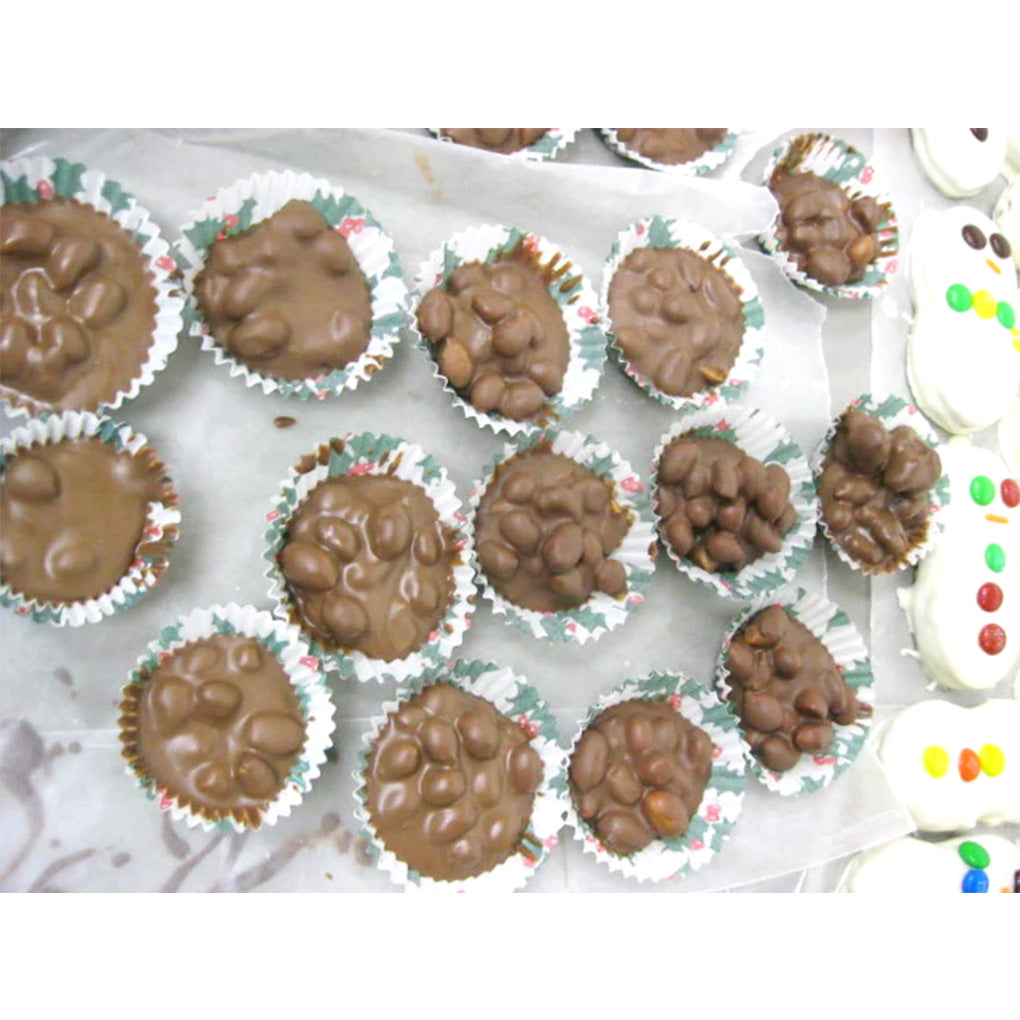 Assorted chocolate peanut clusters in small paper candy cups on a parchment-lined tray, photographed from above.