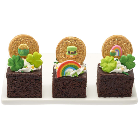 St. Patrick’s Day brownie squares topped with shamrock sugar decorations, rainbow and gold accents, and gold coin-style toppers on a white serving tray.