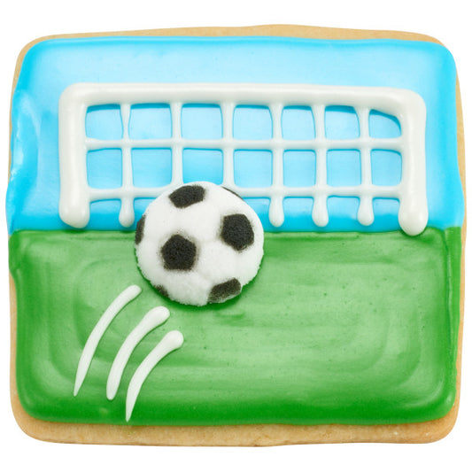 Decorated sugar cookie featuring a green soccer field with a goal and a 3D soccer ball sugar decoration placed in front of the net.