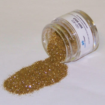 Jar of soft gold Galaxy Glitter Dust labeled “Soft Gold,” spilled onto a white background, gleaming with a delicate metallic glow