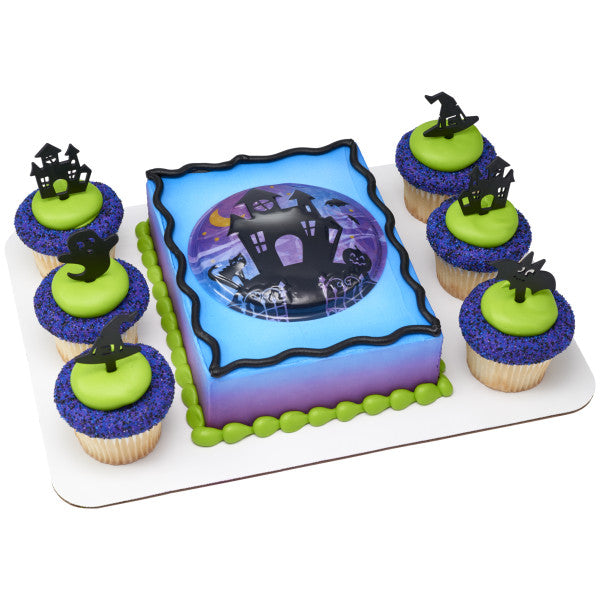 Halloween cake set with purple and green tones, surrounded by cupcakes each topped with different spooky black silhouette picks.