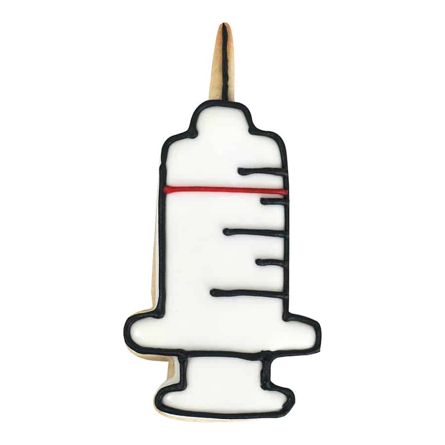 A decorated syringe-shaped cookie with white icing, black outline details, and a red measurement line.