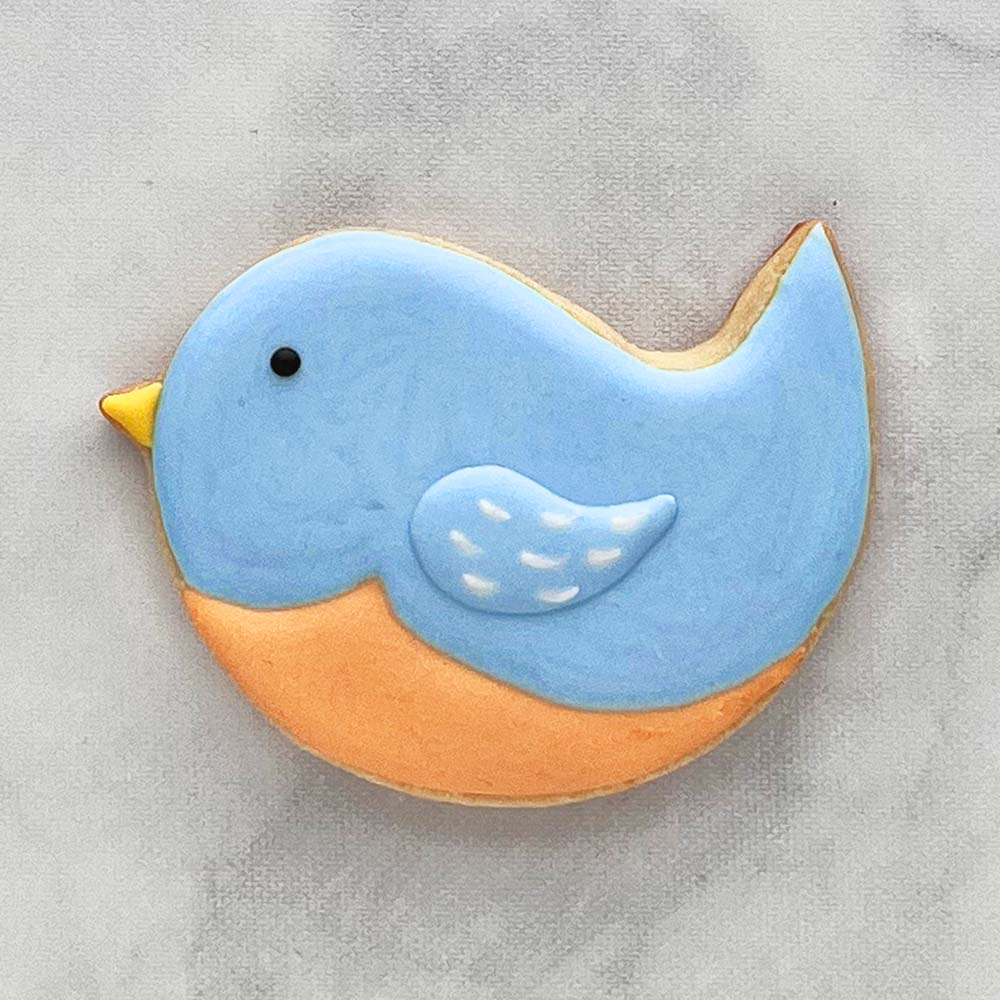 Decorated bird-shaped sugar cookie with blue and orange icing, featuring a small wing and black dot for an eye.