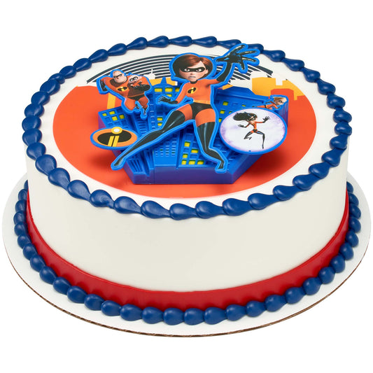 Round white frosted cake with blue and red borders topped with a 3D superhero family cake topper featuring a blue city backdrop and multiple character cutouts.