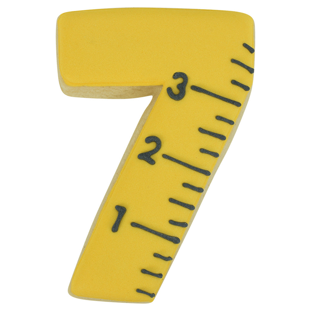 Yellow number 7 sugar cookie decorated with black icing to resemble a measuring tape.